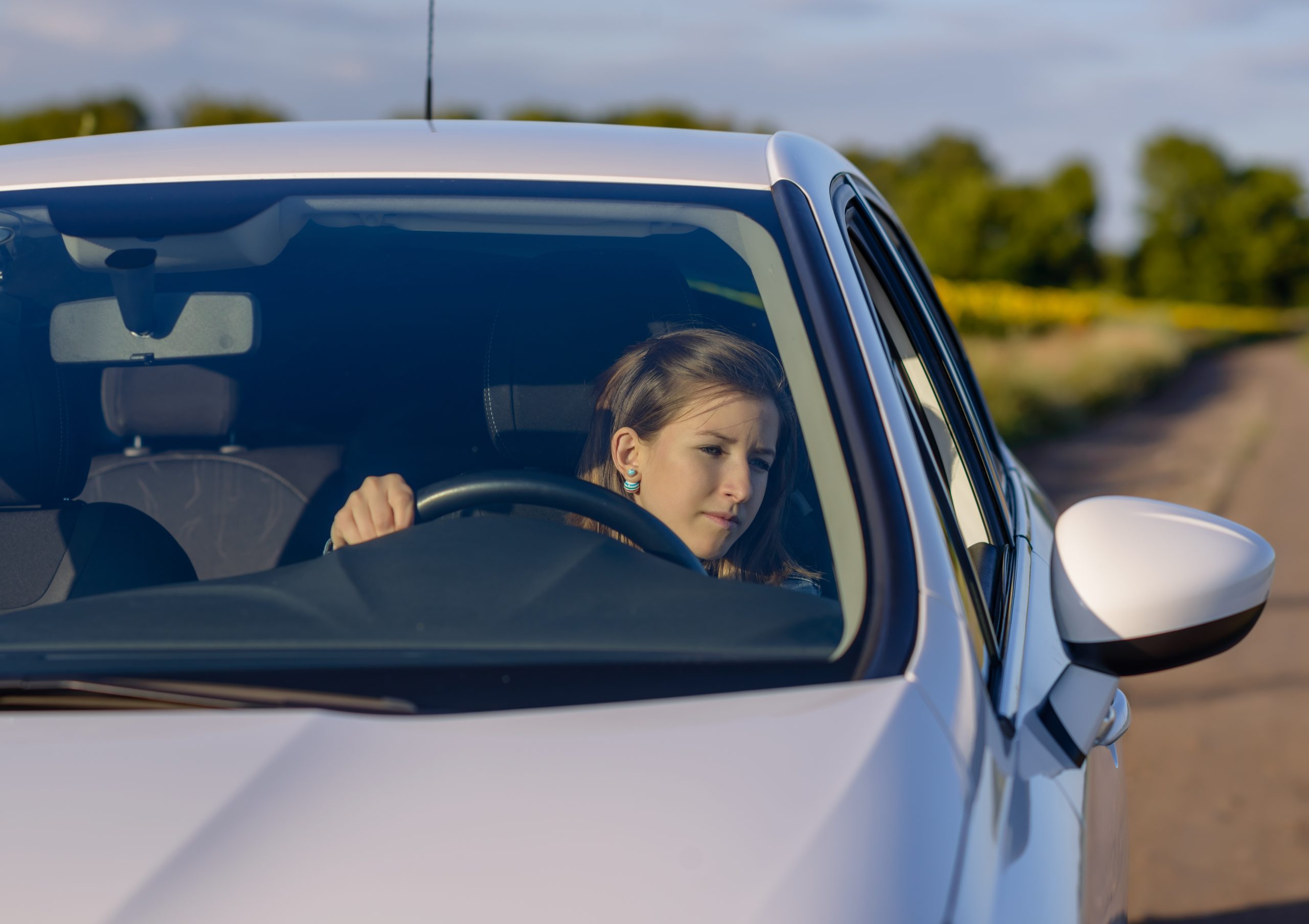 eenage driver checking her side mirror as she pulls away into the street after being parked alongside a rural road